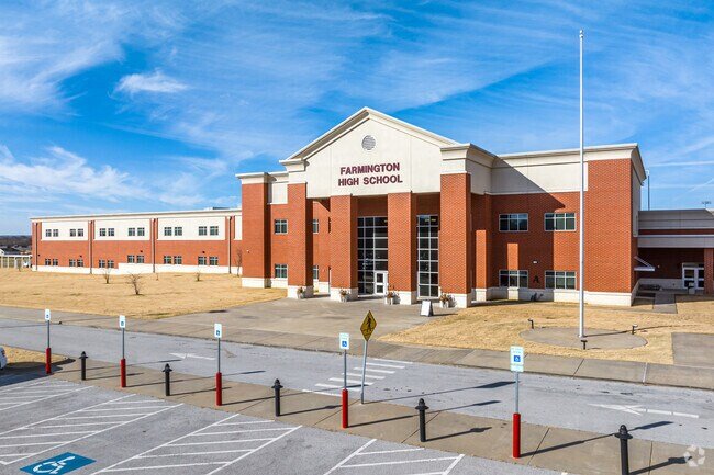 Exterior of Farmington High School in Arkansas, featuring a red-brick school building, main entrance, and parking area.