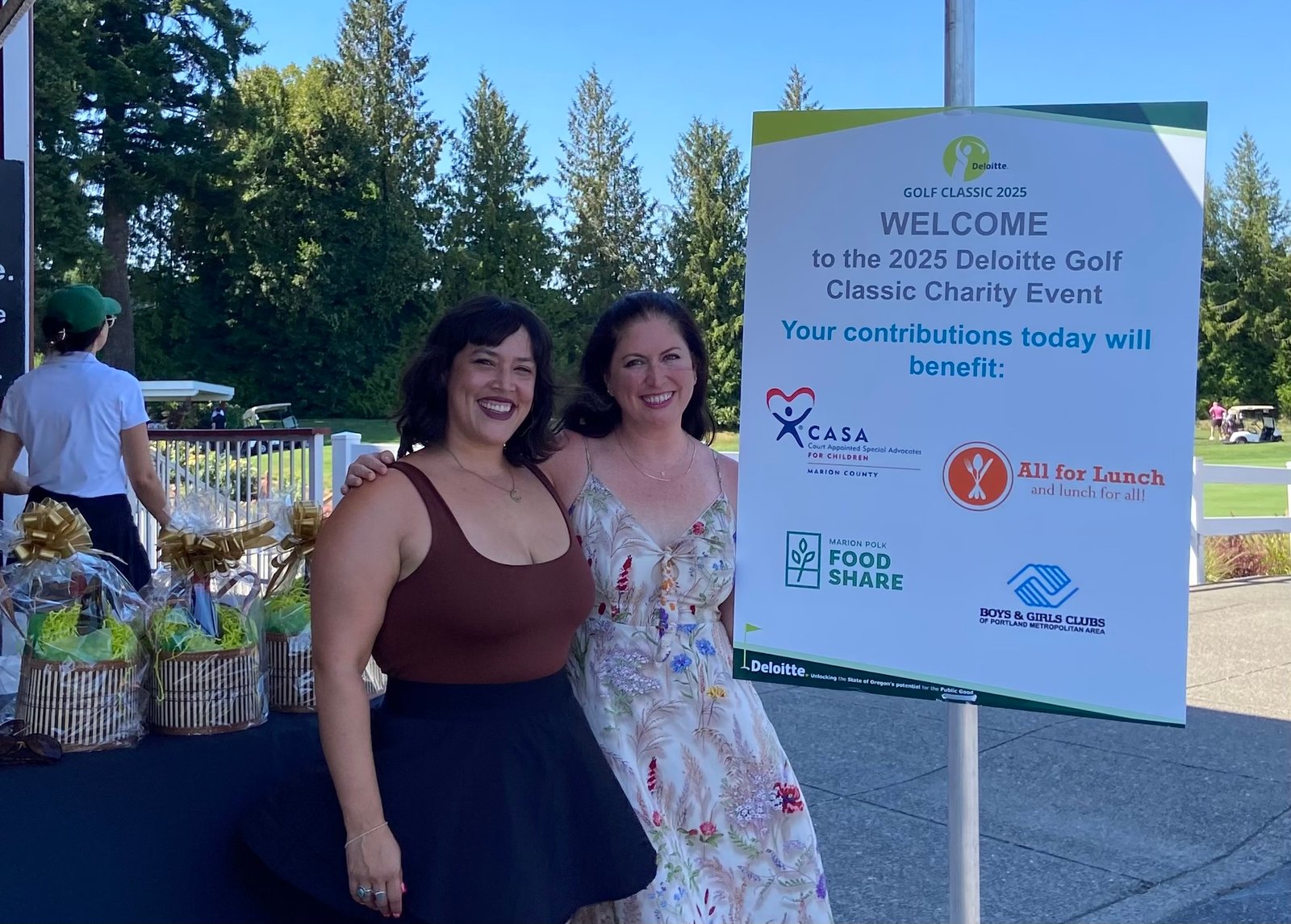 Two All for Lunch representatives standing beside the 2025 Deloitte Golf Classic charity event sign featuring All for Lunch and other nonprofit beneficiaries.