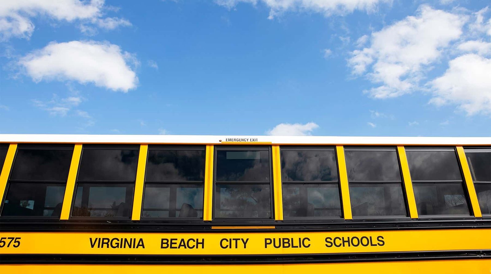 Yellow Virginia Beach City Public Schools bus parked beneath a blue sky with scattered clouds.